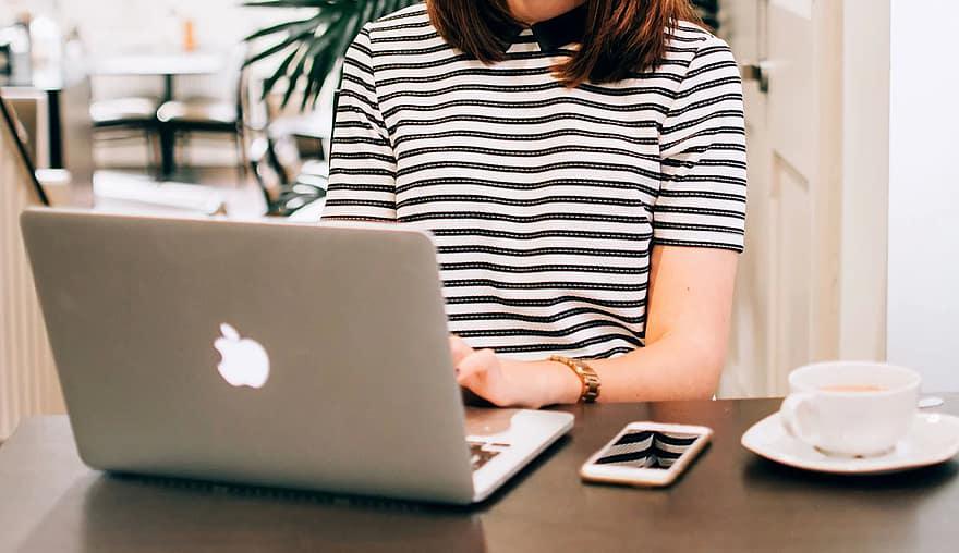 A woman in a black and white striped top carries out SEO outreach prospecting on a MacBook